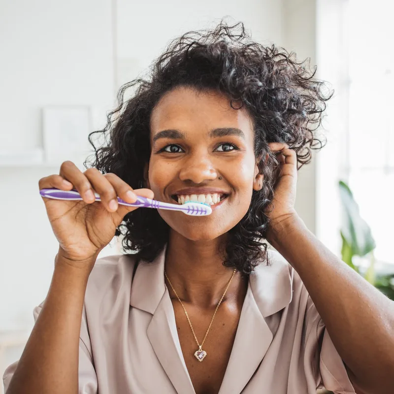 Woman smiling while brushing her teeth in natural light